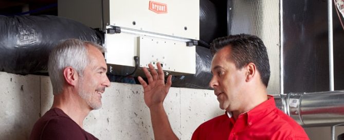 Tech in red shirt explains air ventilators to homeowner in basement.