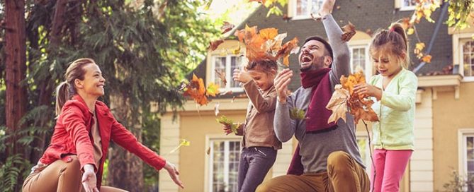 Family plays outdoors with autumn leaves on lawn.