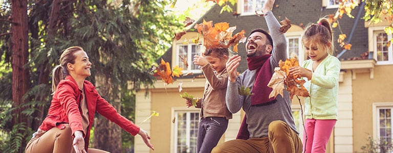 Family plays outdoors with autumn leaves on lawn.