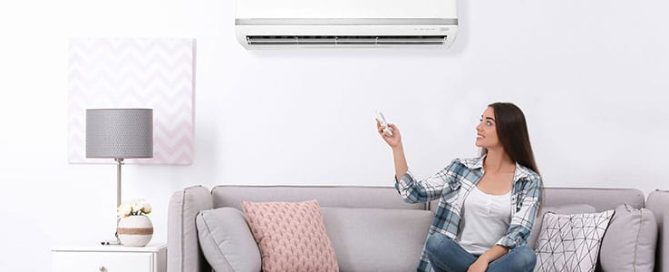 Female homeowner sits on couch and uses remote to activate ductless system.