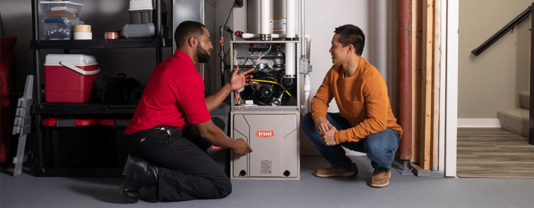 Tech shares regular furnace maintenance plan with homeowner in basement.