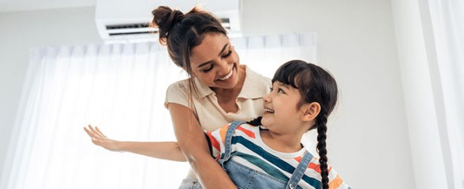 Female homeowner and daughter play in living room after using air conditioner efficiency tips.