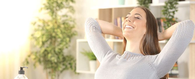 Female homeowner learns how to reduce indoor air pollution and relaxes with arms behind her head.