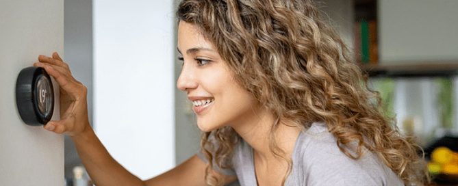 Female homeowner adjusts temperature dial to the recommended thermostat settings for winter.